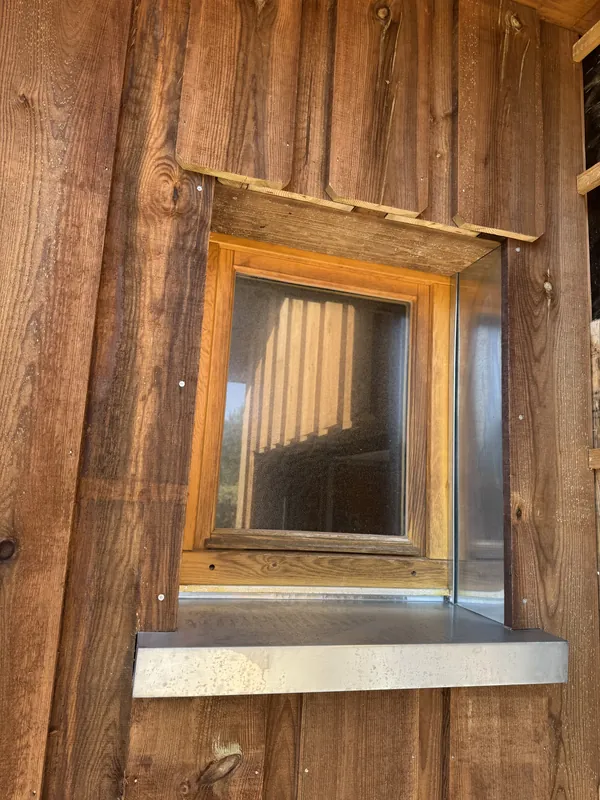 Fenêtre en bois dans un mur de planches, avec un appui et une pièce latérale en métal gris
