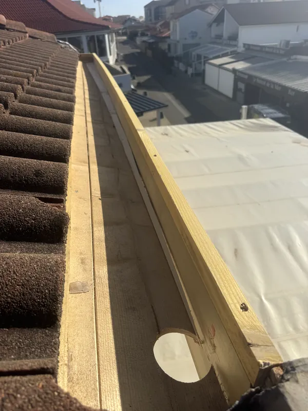 Caisson en bois à trou rond entre un toit de tuiles et une toiture recouverte d’une membrane claire